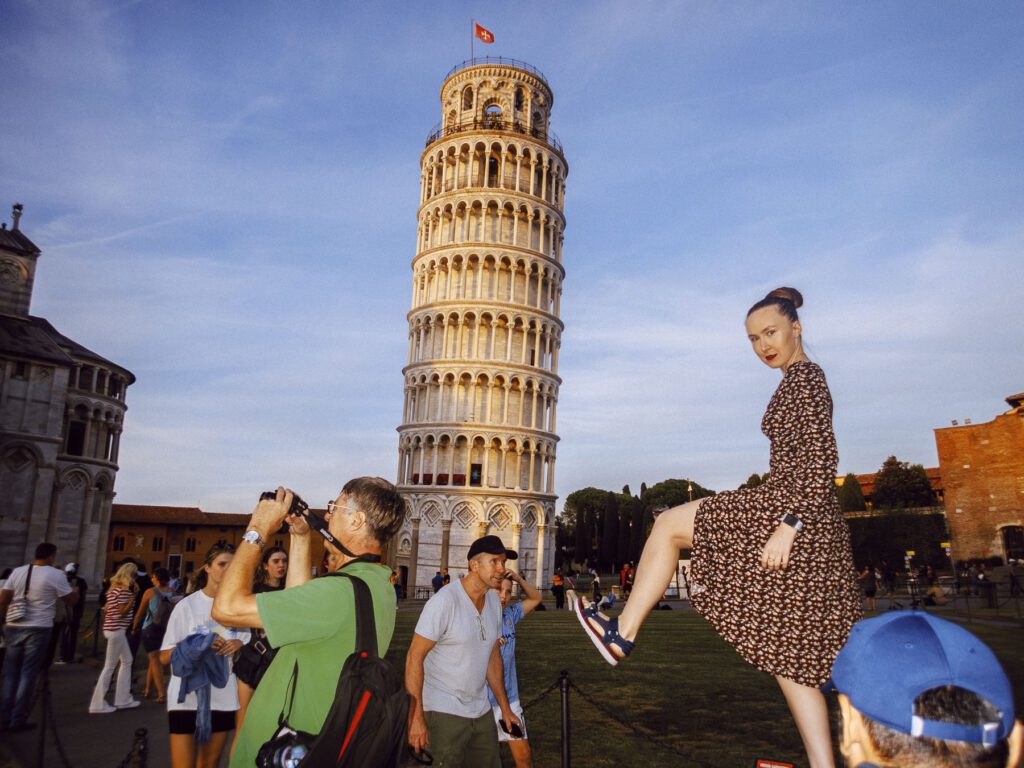 Photograph of a woman in a patterned dress playfully posing as if kicking the Leaning Tower of Pisa.